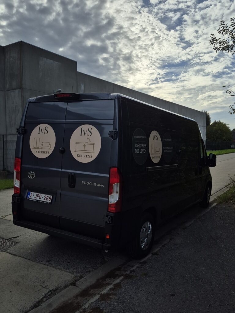 Donkerblauwe bestelwagen van IVS Keukens met merkbelettering, gezien schuin van achteren